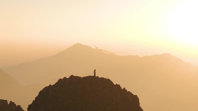 4K cinematic drone shot of a boy standing alone on a mountain top during sunrise in Uttarakhand, India.