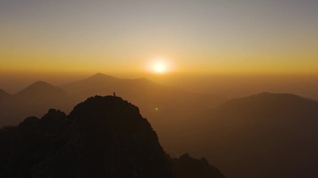 4K aerial sunrise view of a boy standing on a rugged cliff surrounded by Himalayan landscapes.