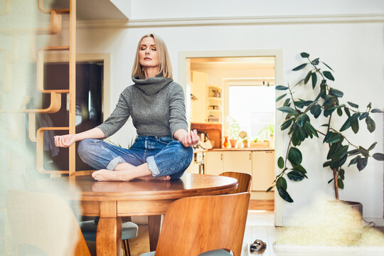 Woman meditating in lotus pose on dining table at home