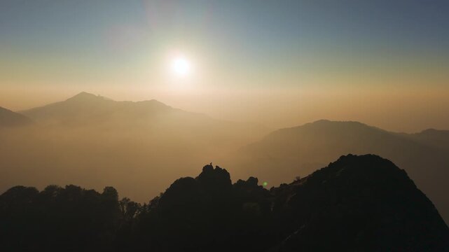 4K aerial sunrise footage of a boy on a rugged mountain summit overlooking the Himalayas.