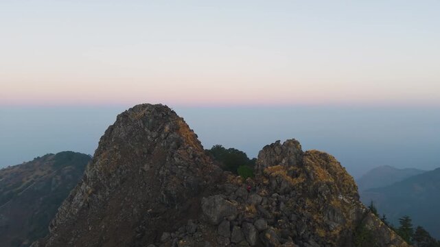 4K aerial drone shot of a boy climbing a rocky mountain during vibrant Himalayan sunrise in Uttarakhand, India.