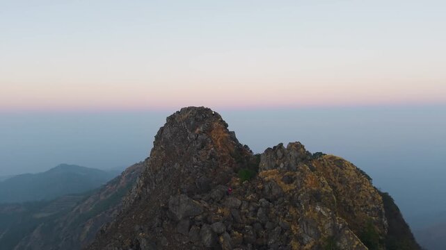 4K cinematic drone footage of a young traveler climbing a rugged mountain peak at sunrise in Uttarakhand.