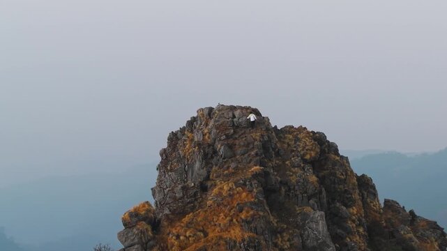 4K scenic drone shot of a traveler ascending a rocky Himalayan mountain at sunrise in Uttarakhand, India.