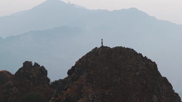 4K cinematic aerial footage of a lone traveler standing on a rocky summit with massive Himalayan layers in the background.