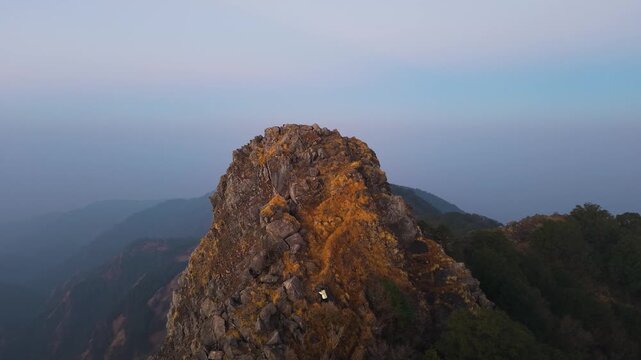 4K drone shot of a young adventurer scaling a rocky mountain during sunrise in Uttarakhand, India.