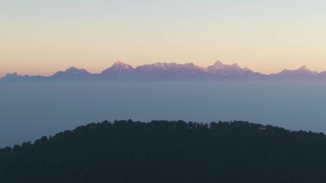 4K drone footage capturing golden sunrise light falling on snowy Himalayan mountain peaks in Uttarakhand, India.