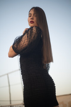Beautiful and sensual young woman in a dress on a building rooftop in the golden hour