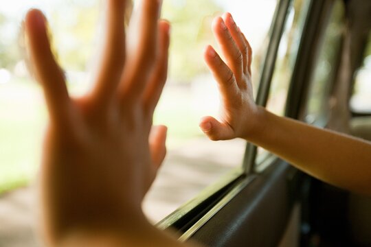 close up of a childs hands pressed against a car window looking outside during a road trip with warm sunlight blur