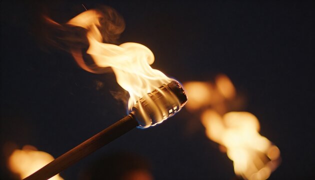 Burning handheld torch wooden handle metal-wrapped head casting warm glow at night, blurred flames