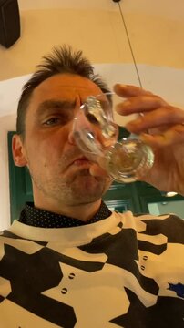 Caucasian man drinking liqueur at bar counter, sampling digestif after espresso, holding small glass and metal teapot on tray, wearing patterned