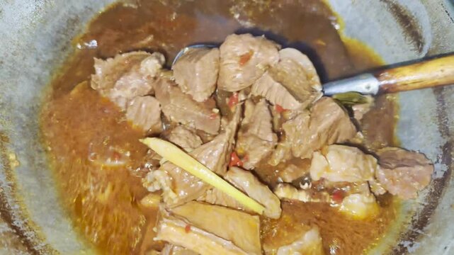 Boiling beef in wok during traditional Indonesian rendang cooking process, authentic Padang cuisine preparation