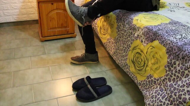 Videoclips de un hombre en el interior de su habitaci&oacute;n, se cambia los zapatos por unas pantuflas c&oacute;modas junto a la cama. La escena transmite un momento cotidiano de descanso y relajaci&oacute;n. 