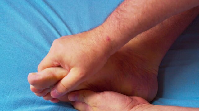 Close-up video of a man massaging his foot to relieve pain and tension after a demanding workday. Captured in soft natural light, highlighting the anatomy of hands and foot movement.
