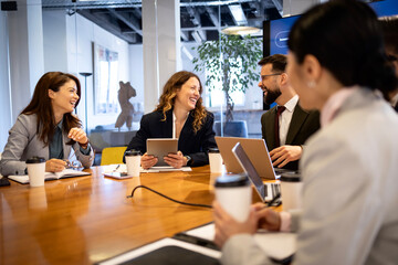 Fototapeta premium Business colleagues laughing and sharing ideas during an informal meeting in a modern office, enjoying successful teamwork