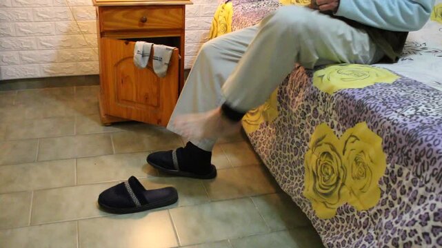 El hombre en su habitaci&oacute;n cambi&aacute;ndose las medias y coloc&aacute;ndose unas pantuflas de descanso al regresar del trabajo. La escena muestra un momento cotidiano y relajado dentro del hogar.