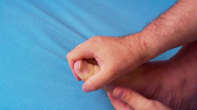 Close-up video of a man massaging his foot to relieve pain and tension after a demanding workday. Captured in soft natural light, highlighting the anatomy of hands and foot movement.