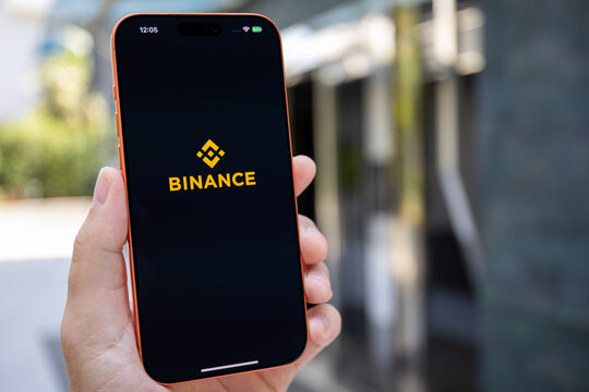 Mans hand holding phone Apple iPhone 17 Pro Max Cosmic Orange outdoors displaying application cryptocurrency exchange Binance on screen smartphone