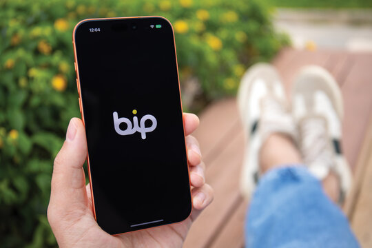 Man hands holding phone Apple iPhone 17 Pro Max Cosmic Orange outdoors displaying application messenger BiP logo on screen