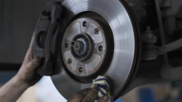 Close Up of Mechanic Hand Cleaning and Wiping a Car Brake Disc Rotor with a Rag in an Auto Repair Shop