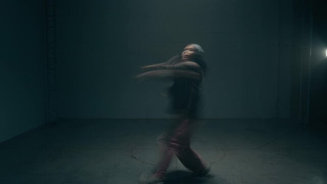 Wide angle shot of young female dancer dancing expressive hip hop freestyle in dark underground studio with choppy motion blur effect, copy space