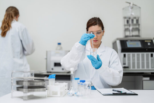 Professional female scientist stirring liquid sample in beaker with glass rod at modern laboratory. Commercial cosmetic chemistry business and medical innovation for sustainable development concept.