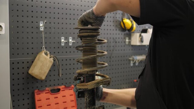 A mechanic repairs car shock absorbers at a service station. He removes the spring to repair it. The process of repairing a car at an auto repair shop.