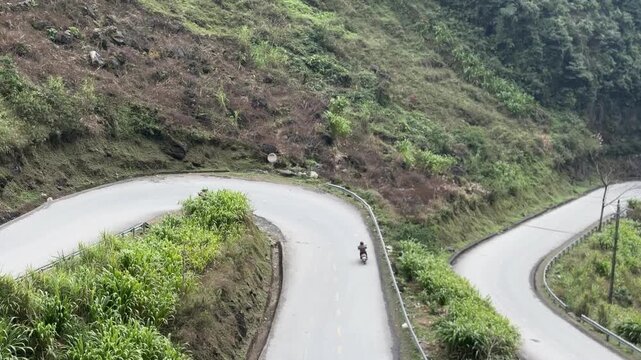 Winding S shaped mountain road with steep switchbacks and motorcyclists riding through rugged landscape at Tham Ma Pass in Ha Giang, northern Vietnam