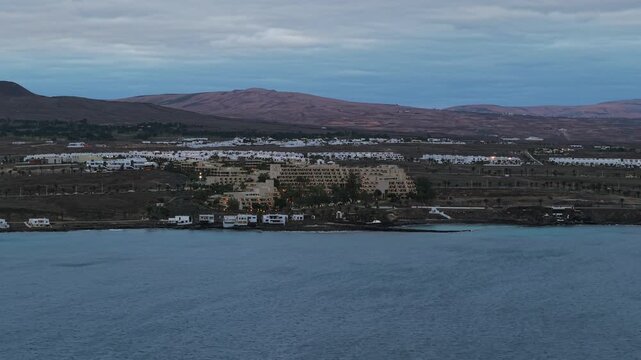 Resort town of Costa Teguise on volcanic coast of Lanzarote at blue hour, Canary Islands, Spain. Aerial drone lateral view, copy space