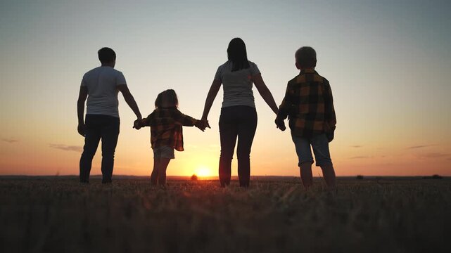 Family holding hands at sunset. Family, silhouette, holding, hands together, team, sunset, park. Team of football players together at the park at sunset. The photo is of a lifestyle family holding.