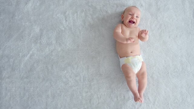 A healthy newborn baby in a diaper without clothes, top view.  Full  length . Happy newborn boy lies on a blue blanket and actively moves his arms and legs.  Cute baby with blue eyes . Slow motion.