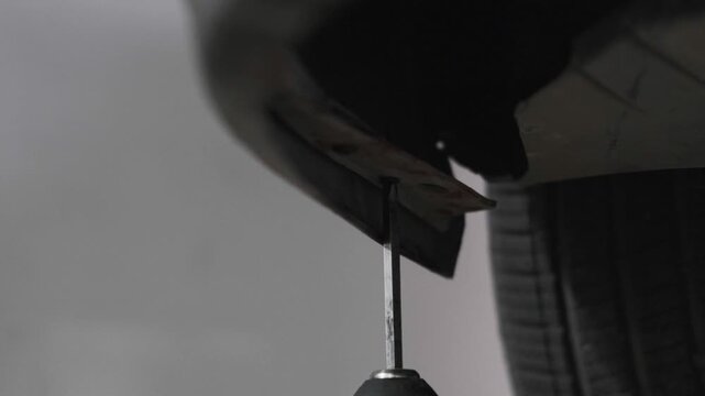 Close Up of Using a Cordless Electric Drill to Fix a Car Bumper Underbody Panel in an Auto Repair Workshop