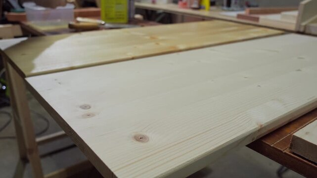 Close up of a wide paintbrush applying clear gloss lacquer to a clean wood board, revealing the natural grain pattern.