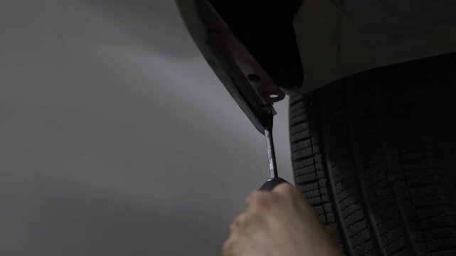 Close Up of Using a Cordless Electric Drill to Fix a Car Bumper Underbody Panel in an Auto Repair Workshop