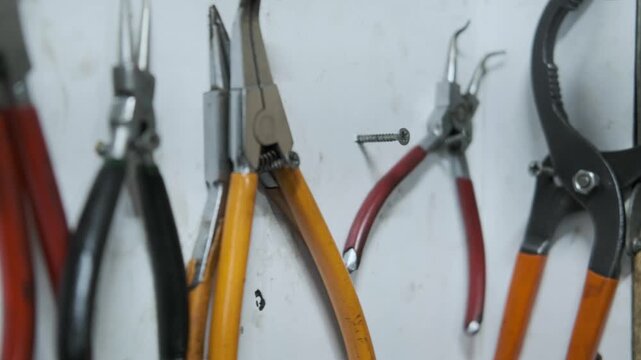 Various Types of Pliers and Hand Tools Hanging on a White Organizer Board in a Mechanical Workshop