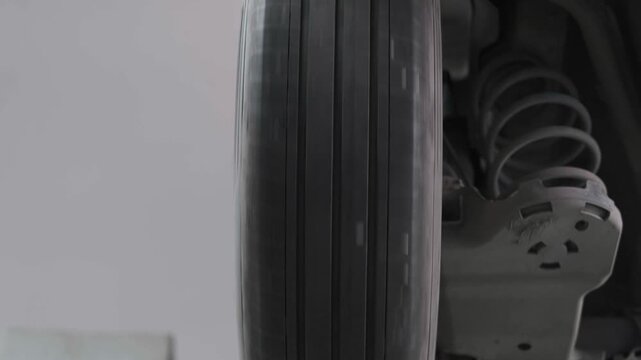 Spinning Car Wheel Tire with Motion Blur and Suspension Coil Spring on a Lift in Auto Service Workshop