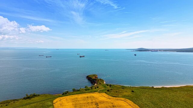 Green Coastal Field Rocky Peninsula Cargo Ships Black Sea. A green field with a yellow crop patch meets the Black Sea coast where cargo ships anchor offshore.