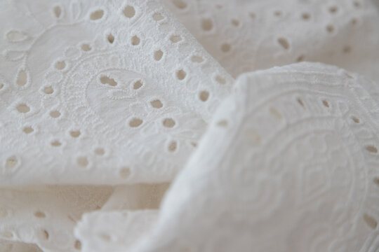 White cotton fabric with broderie anglaise or cutwork embroidery, ideal for creative backgrounds, banners, and textile design. Selective focus, close up