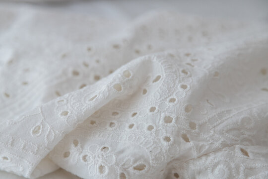 White cotton fabric with broderie anglaise or cutwork embroidery, ideal for creative backgrounds, banners, and textile design. Selective focus, close up