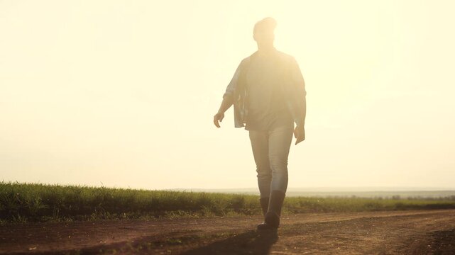Man walking down dirt road. Silhouette of farmer walking in a field. Farmer working on a field lifestyle in evening. A individual strolling along a unpaved path.