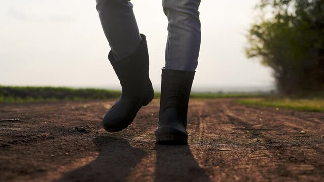 A person walking on a dirt road. Farmer goes on a road lifestyle at sunset. Farmers walk close up on their legs in agriculture. An individual strolling along a dusty path.