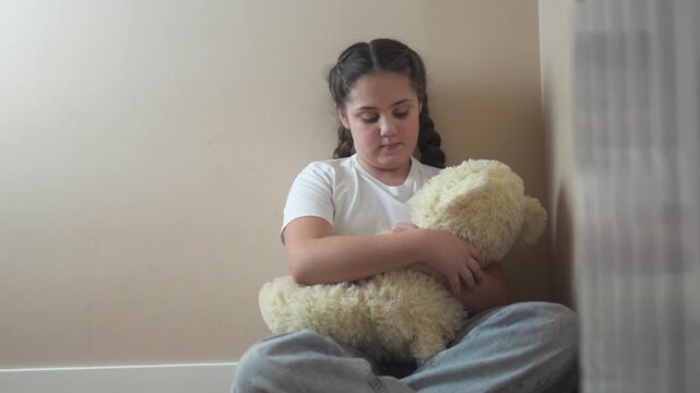 Young girl sitting on the floor with teddy bear. Teddy bear punished by sad corner. Teenage girl is traumatized by a violent attack by a teenager. A young girl is seated on the floor lifestyle with a.