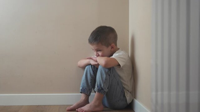Young girl sitting on the floor. Sad child sits on a corner and is punished. A teenage lifestyle girl is traumatized by a violent incident. A little girl sitting on the ground.