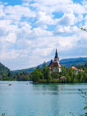 Obraz premium Beautiful day with blue sky, sunshine and emerald green water of Lake Bled and Bled Castle and the view of Church of the Assumption of the Blessed Virgin Mary on the island in the middle of the lake 