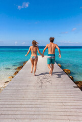 Obraz premium A young couple in swim wear running on a jetty to jump into the Caribbean Sea. Creation supported by generative AI