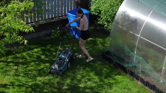 A woman working in the garden with a lawn mower. A woman mows the grass in the yard; a woman tends to the lawn in the spring. A woman and gardening.