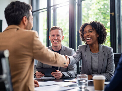 Happy diverse business partners shaking hands after a successful meeting in a sunlit modern office setting.