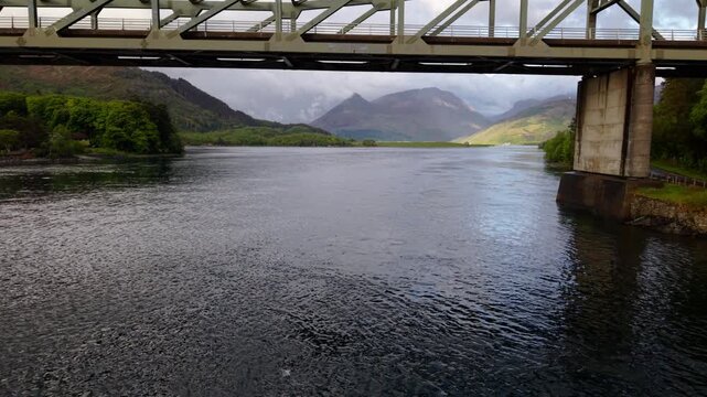 Drone flies slowly back and up from Ballachulish Bridge with stunning light on Glencoe seen in the background.