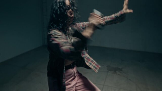 Cinematic zoom out shot of young female dancer pressing button turning on wireless speaker and dancing hip hop freestyle choreography in dark industrial studio, copy space