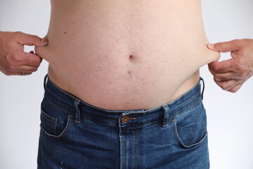 Naklejka premium Overweight man with belly in blue jeans. Concept of obesity, unhealthy lifestyle, excess weight and diet problems. Isolated on white background.