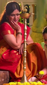 Decorating flower rangoli around samai, Indian young girl senior mother in traditional wear joyfully preparing for Hindu festival Diwali celebration indoors in evening with diya and colorful design